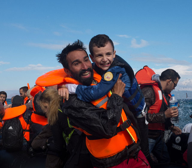 On 30 September,volunteer Kinan Kadouni, 26, and the boy he is carrying, both refugees from the Syrian Arab Republic, laugh amid other newly arrived refugees, and the volunteers helping, following their arrival on the shores near the village of Skala Eressos, on the island of Lesbos, in the North Aegean region. 