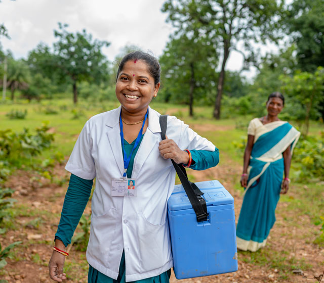 ANM and Mitanin carry vaccine carriers through difficult terrain for VHSND session. Village Ghotpal, Dantewada, Chattisgarh