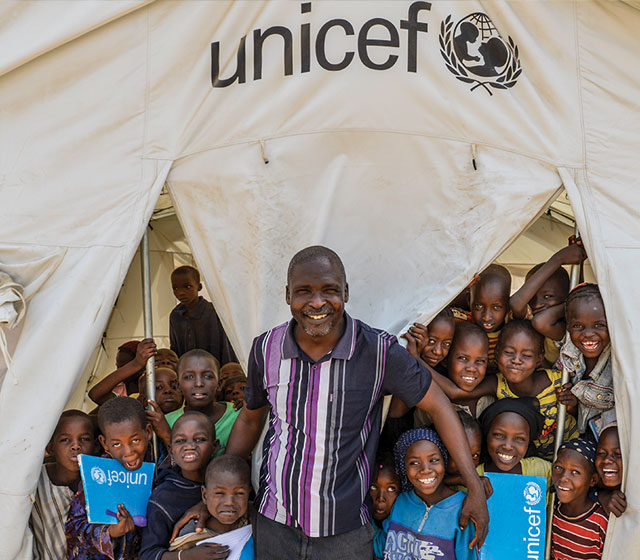 On 25 March, Amos Asaai, a volunteer teacher, stands with his students at the entrance to a UNICEF-provided tent classroom in the Gire 2 camp for internally displaced people, near Yola, the capital of Adamawa, a state in the country’s north-east.