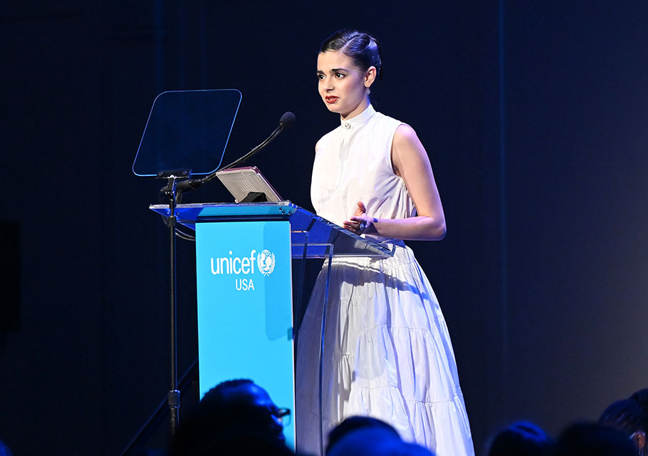 Aria Mia Loberti in a white dress standing at the podium