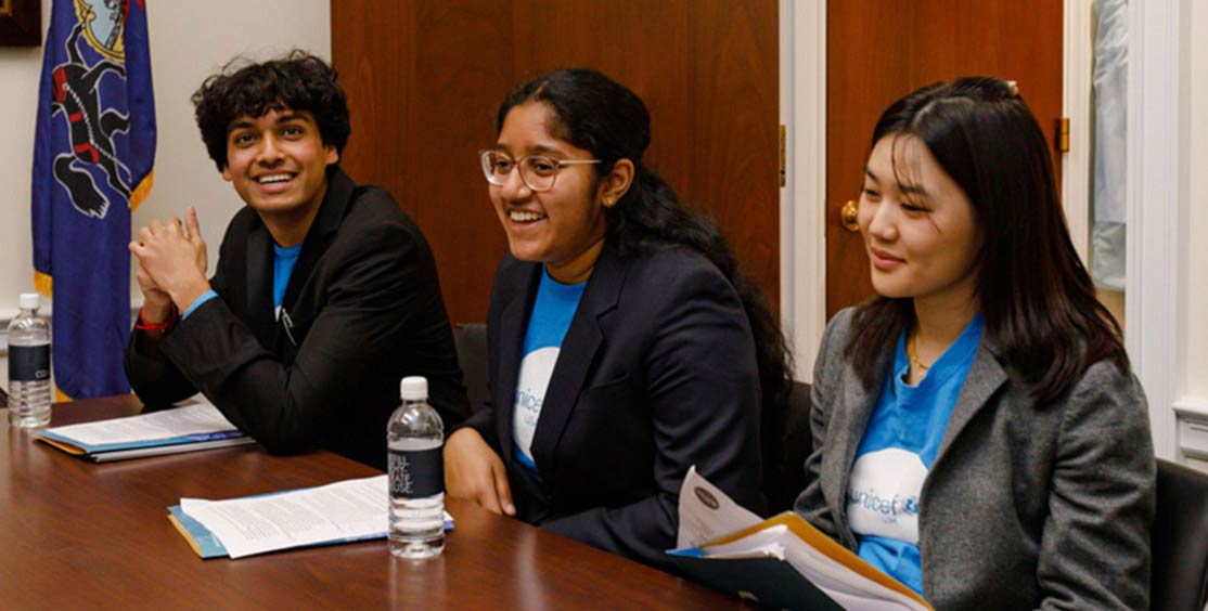 Three club members are shown wearing blazers over UNICEF USA t-shirts as they sit in a conference room with their advocacy or briefing materials in front of them.