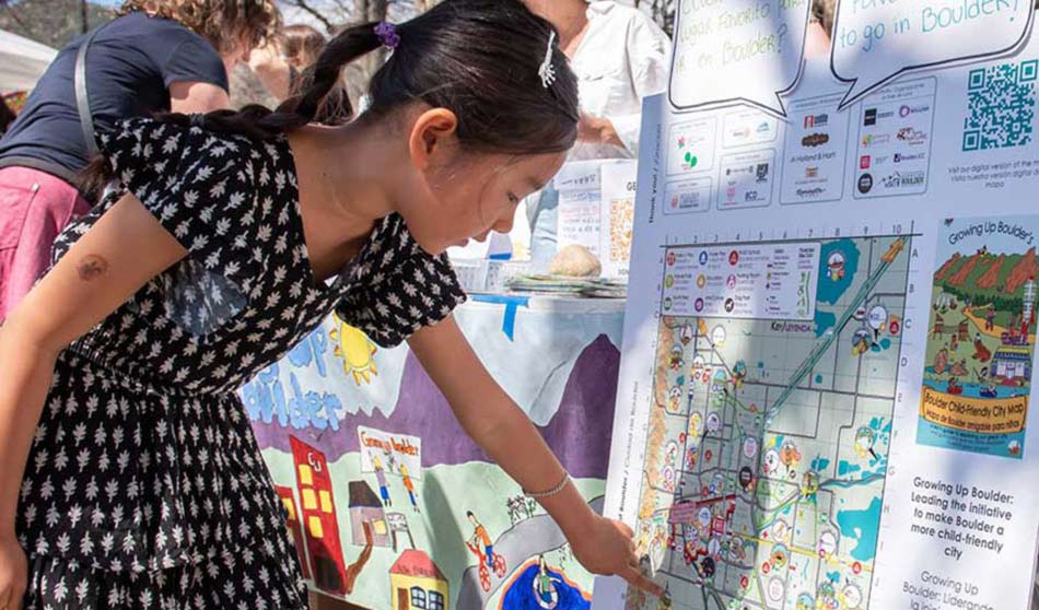 A young girl points to items on a map, which signify child-friendly efforts in her town.