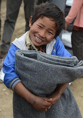 A smiling boy proudly holds a thick blanket bundle he was just handed outside.