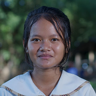 A girl in a red shirt with hair tied behind her head, smiling at the camera.