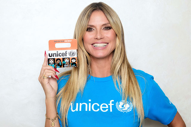 Heidi Klum wears a blue UNICEF t=shirt, and holds up a yellow UNICEF Trick-or-Treat box.