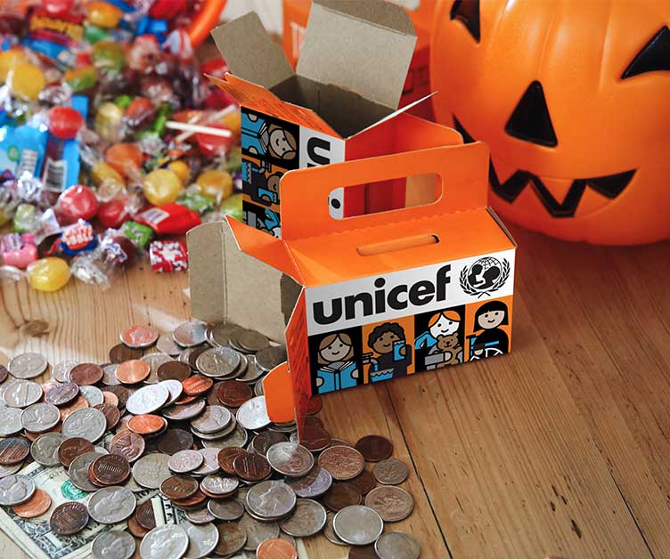 An orange Trick-or-Treat for UNICEF box, among candy and a trick-or-treat jack-o-lantern