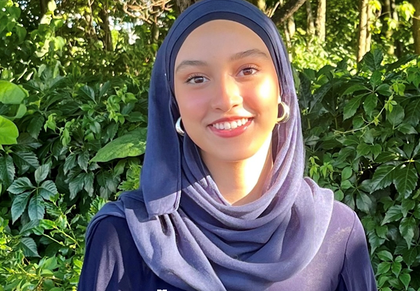 Portrait of Sophia Dasser, smiling in a headscarf standing in front of greenery outside