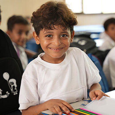 A child at a desk in a classroom smiles while studying a lesson.