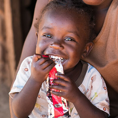 A smiling child eats from a packet of nutritional food, and is now healthy again.