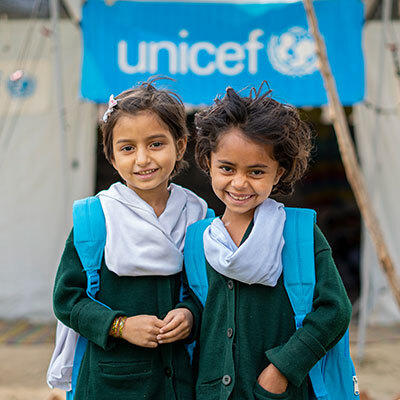 Two young girls pose happily in front of a UNICEF tent at a displaced person's camp.