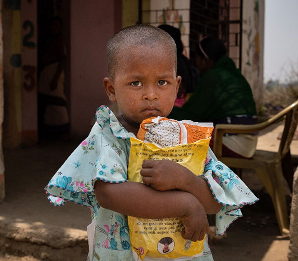 Boy in front of a school holding supplies.