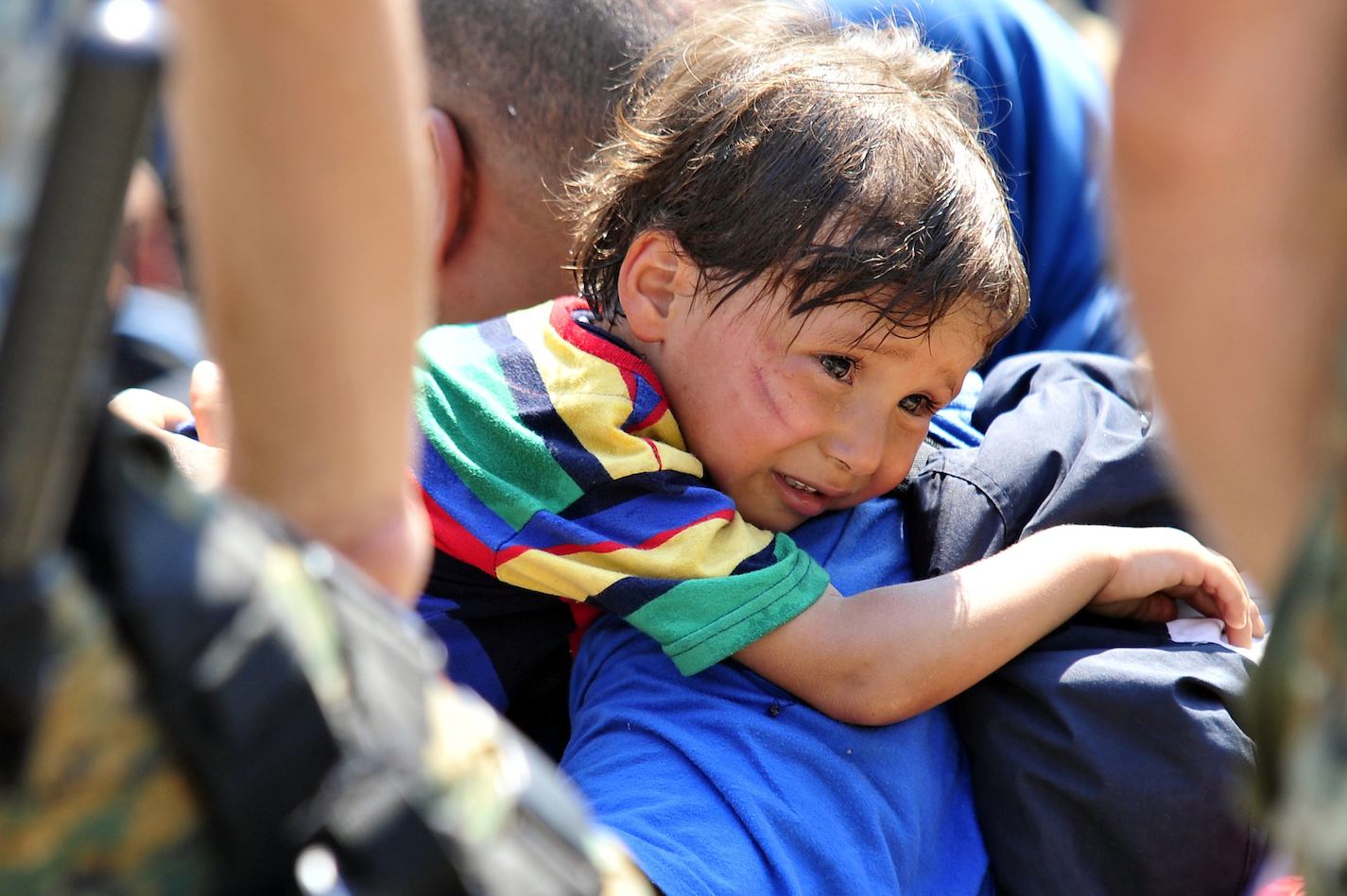On 26 August, a distressed migrant child rests over a shoulder in a Macedonian town on the border with Greece.