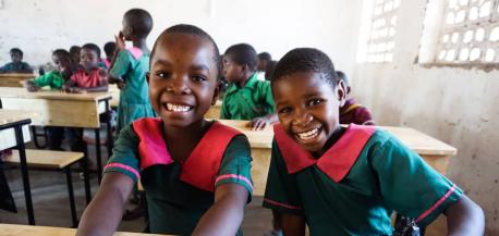 Two smiling students sit side by side at one of the brand new desks delivered to Mkombezi Primary School in Malawi's southern Mangochi region by Kids In Need of Desks (K.I.N.D.)