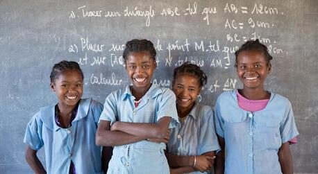 Four smiling female students in front of a classroom blackboard