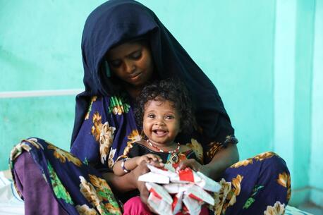 A mother holds her smiling daughter as she receives Ready-to-Use Therapeutic Food (RUTF) from a UNICEF-supported health worker in Ethiopia.