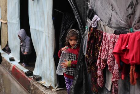 In Rafah, Gaza Strip, a girl stands in the rain holding an empty water bottle.