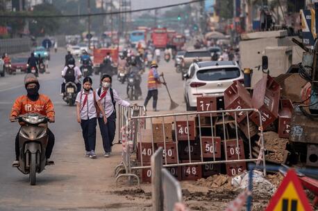 People wearing masks navigate through a dusty construction area on Kim Dong Street, Hai Ba Trung District, Hanoi, Vietnam.