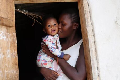 In Sierra Leone, a mother holds her smiling baby in a doorway.