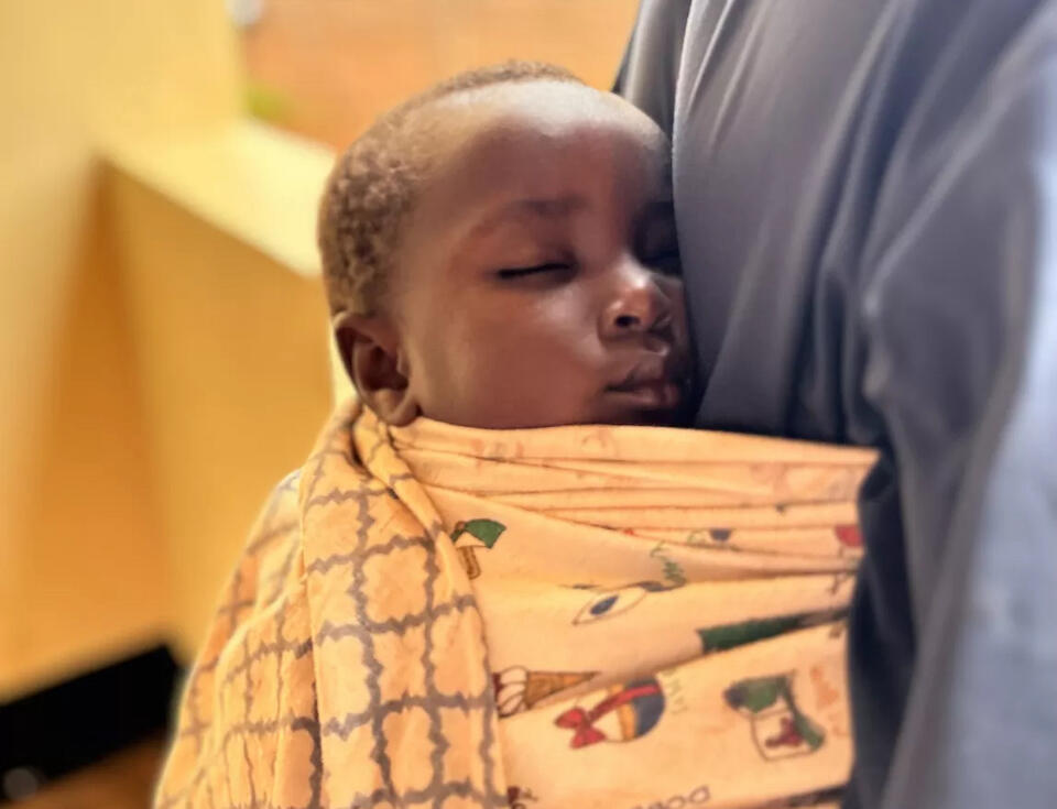 Israel, a 19-month-old boy from Burundi who received treatment for severe wasting after being diagnosed by a UNICEF-supported health worker at a refugee camp in Tanzania, rests against his mother, swaddled in a blanket.