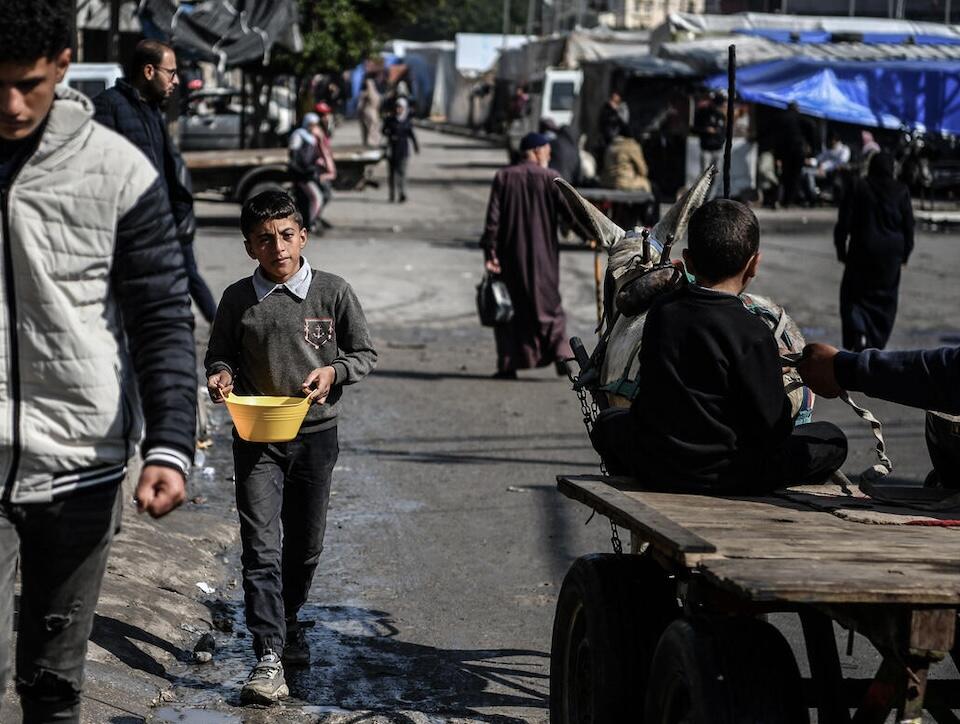 Muhammad, 11, walks the street carrying a bowl of beans he is bringing back to the tent in Rafah, south of the Gaza Strip, where he lives with his mother and siblings.