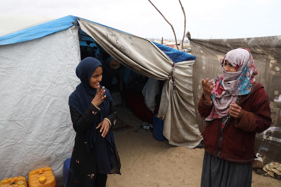Duha, 14, signs with her mother, Iman, in front of their tent in Rafah, southern Gaza Strip.