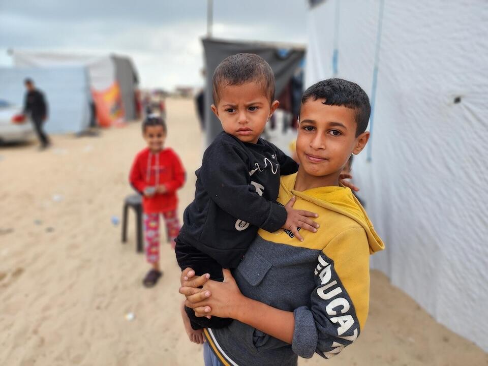 Mohammed, 14, holds his 2-year-old brother Khaled in front of their tent in al-Mawasi, Gaza Strip.