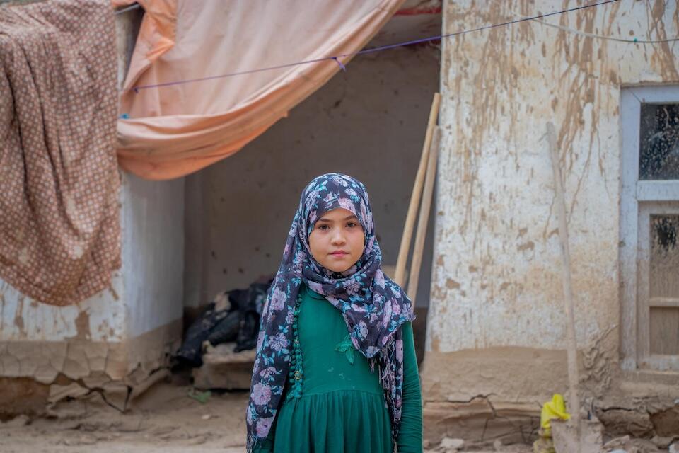 On May 16, 2024, 10-year-old Hosna stands outside her house, which was damaged during recent flash floods in Baghlan province, Afghanistan.