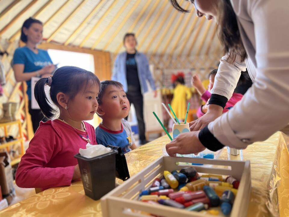 A teacher helps two kindergarten students start on an art project inside a UNICEF-supported mobile ger kindergarten in Altanbulag, Tuv province, Mongolia.