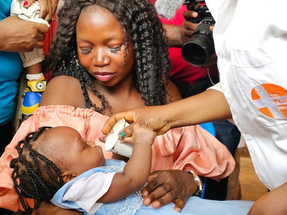 In January 2024, a mother holds her 6-month-old daughter before she is vaccinated against malaria. 