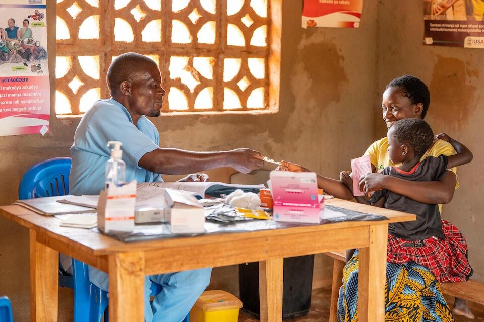 On Jan. 29, 2024, health worker James Chinomba hands antimalarial medication to a mother at Chipili Community Center, Lilongwe District, Malawi.