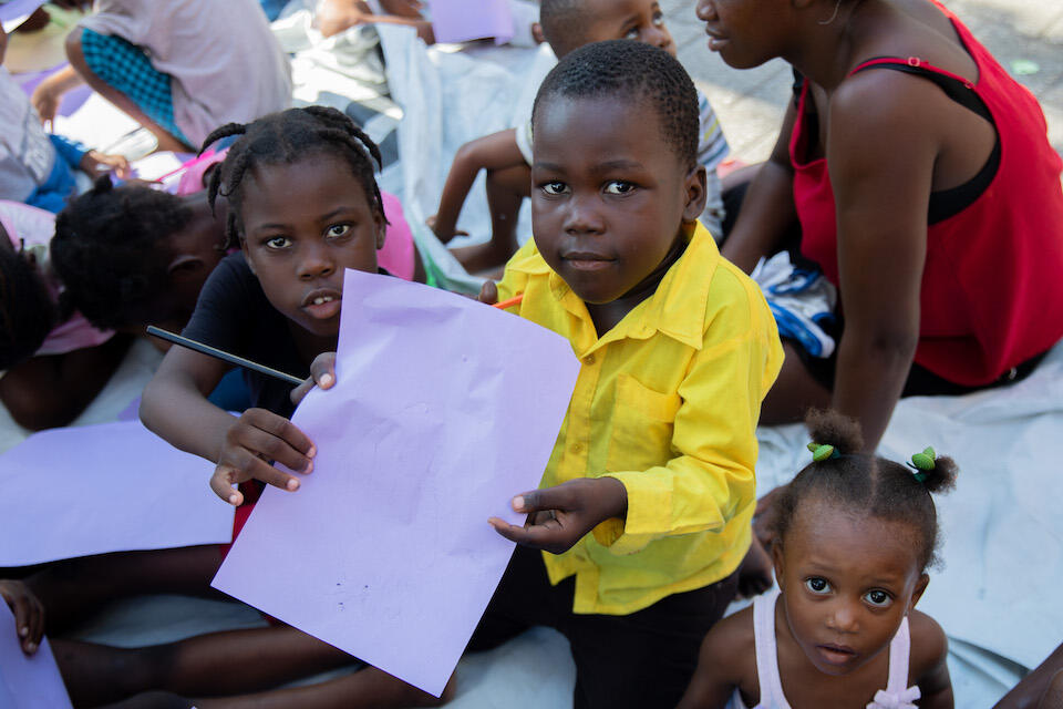 Three children show their artwork created during a psychosocial support session in Port-au-Prince, Haiti, where UNICEF and partners are providing emergency services to those caught in the country's humanitarian crisis.