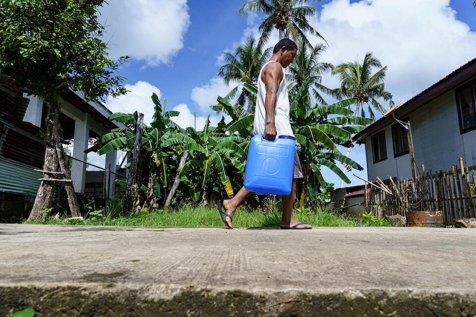 A man in the Philippines carries drinking water from a water refilling station provided by UNICEF through its WASH program following the severe and widespread damages caused by Super Typhoon Odette (Rai).