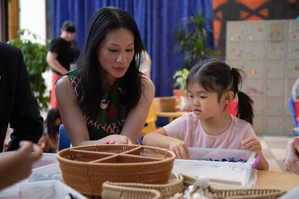 UNICEF Ambassador Lucy Liu sits at a table with a young girl during a UNICEF program visit.