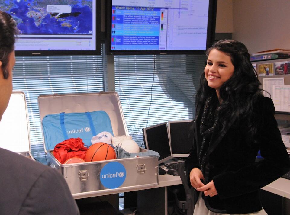 Selena Gomez stands next to a UNICEF recreational kit, a box of supplies that is often sent to children in emergencies.