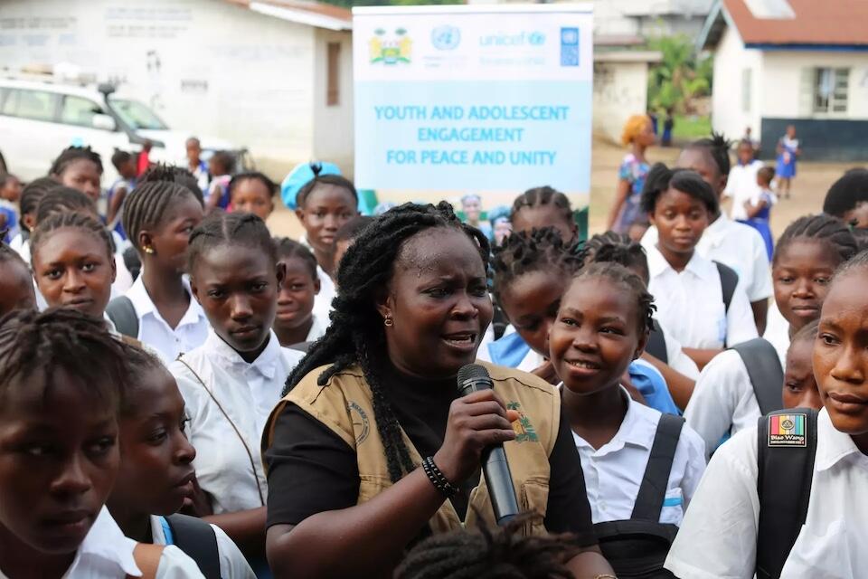 Isatu Kamara, an Alternative Disputes Resolution and Outreach Officer of the Legal Aid Board, is flanked by a group of enthusiastic adolescent boys and girls at the Baptist Junior Secondary School in Makeni, northern Sierra Leone, where UNICEF supports efforts to empower youth with life skills and educate them on violence prevention and peace building.