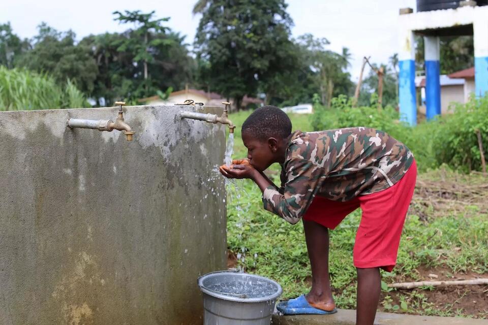 A boy in Sierra Leone drinks from a water tap.