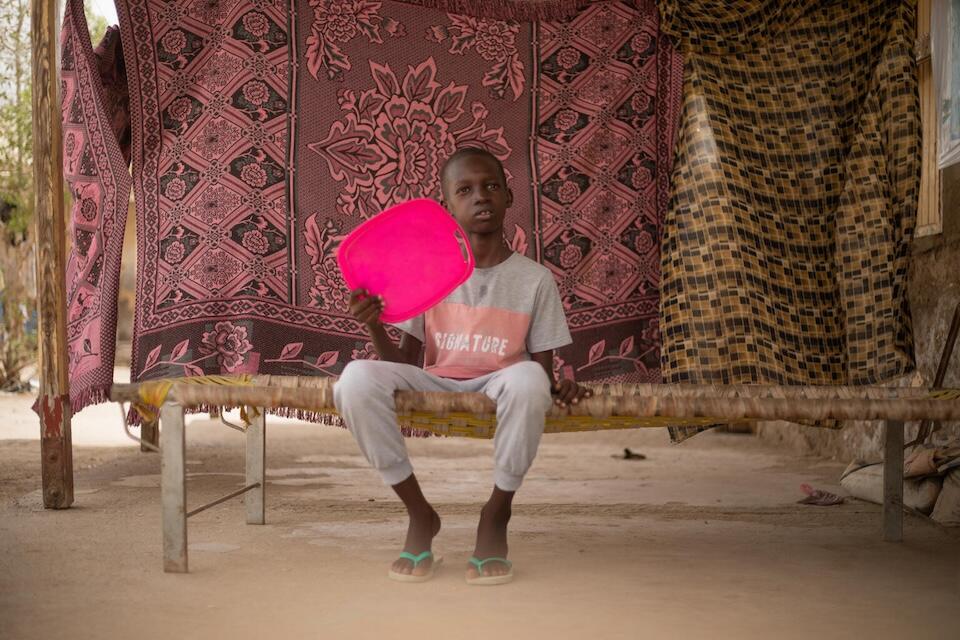 Ali, 10 years, sits under a roof and uses a plastic box lid to fan himself to cool down in Port Sudan.