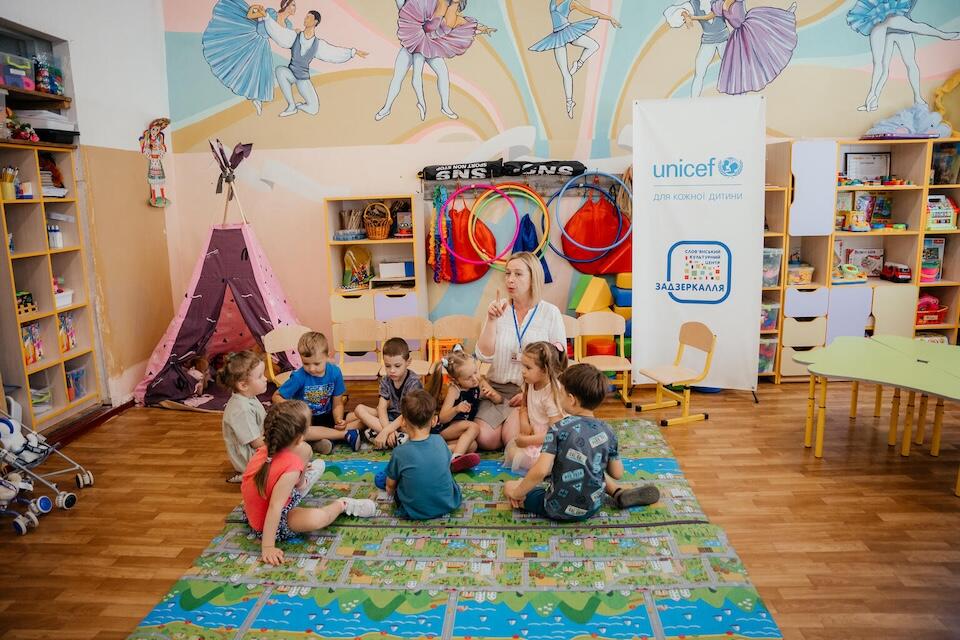 In Mykolaiv, Ukraine, preschoolers sit on the floor around their teacher during class at a UNICEF-supported early childhood education support center.