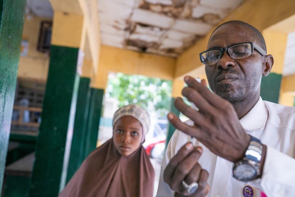 Safiyya, 10, watches as Alimudeen Mohammed, ward in charge at the Katsina Kofar Marusa Maternal and Child Health Clinic, prepares a human papillomavirus (HPV) vaccine in Katsina, Nigeria on May 30, 2024. 