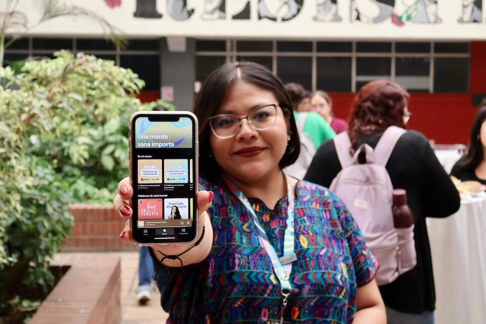 A student at San Carlos University in Guatemala City, Guatemala, holding a phone tuned to a UNICEF podcast on Spotify offering mental health support.