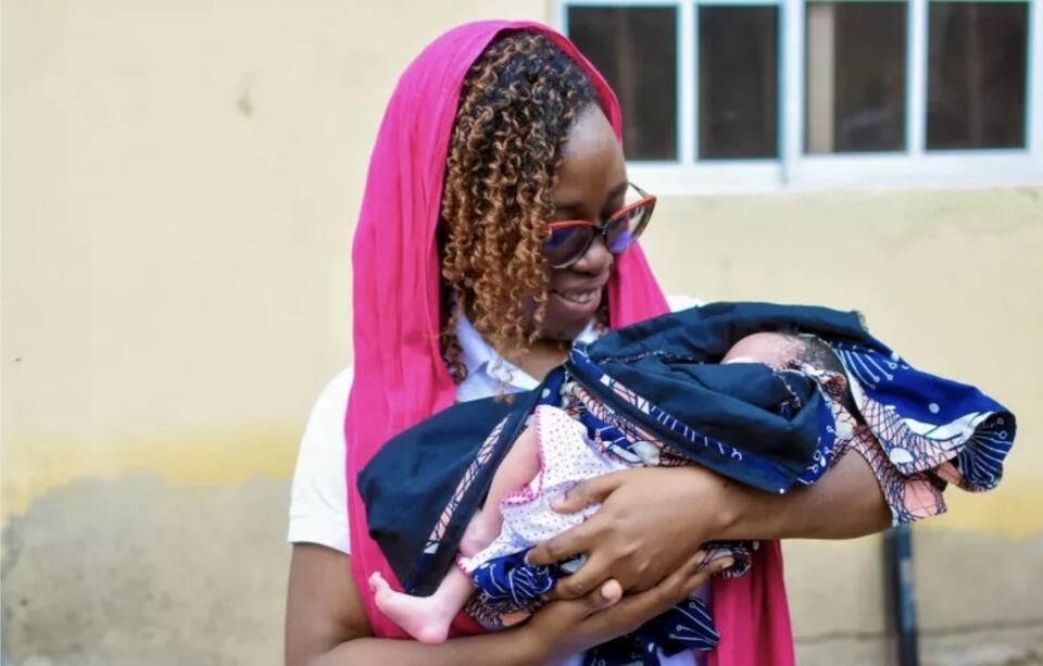 Anike Alli-Hakeem, Communication Officer, UNICEF Nigeria, holding a newborn baby at a UNICEF-supported camp for families displaced by flooding in Maiduguri, Nigeria.