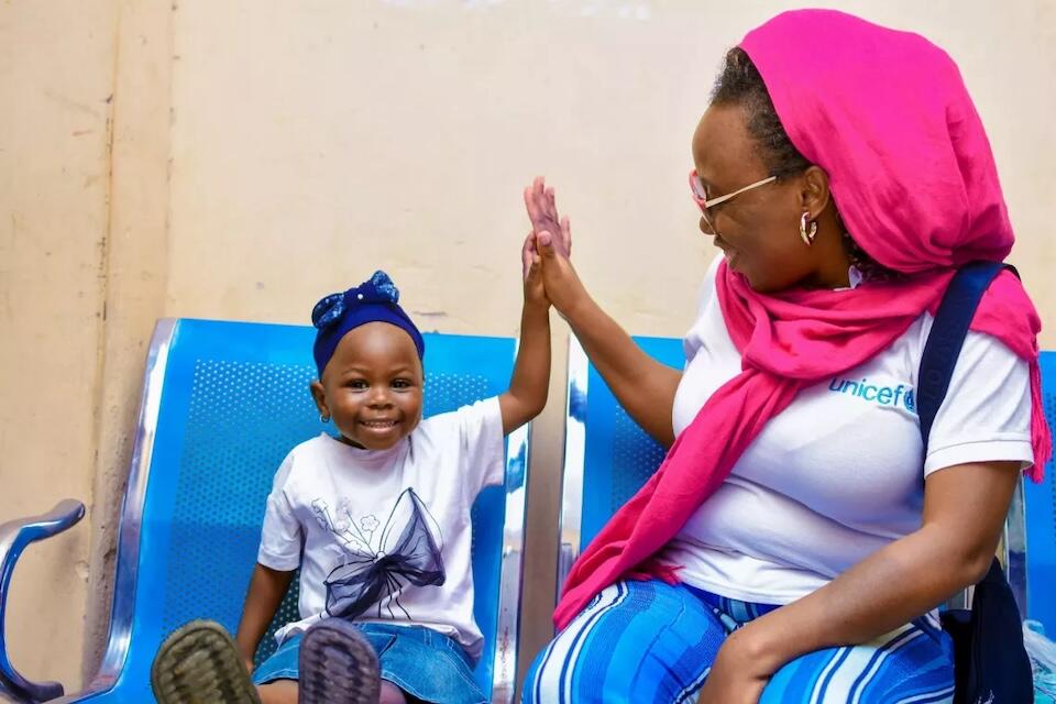 UNICEF staff high-fives a young girl at a UNICEF-supported displacement camp for families affected by flooding in Maiduguri, Nigeria. 