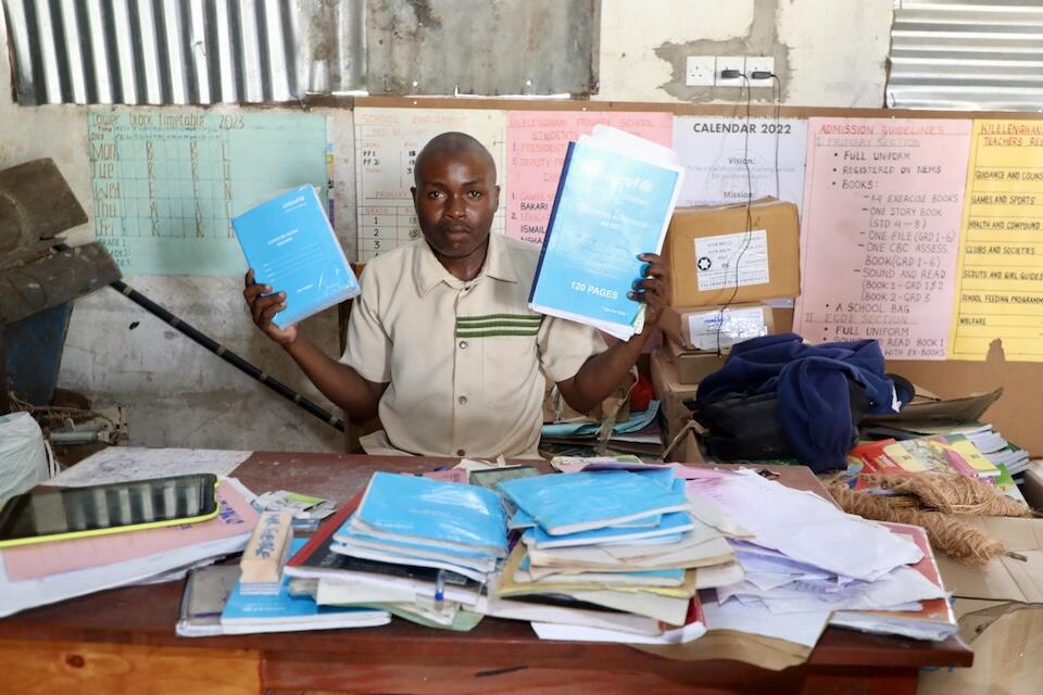 A teacher holds up notebooks delivered by UNICEF to Kilelengwani Primary School in Kenya.