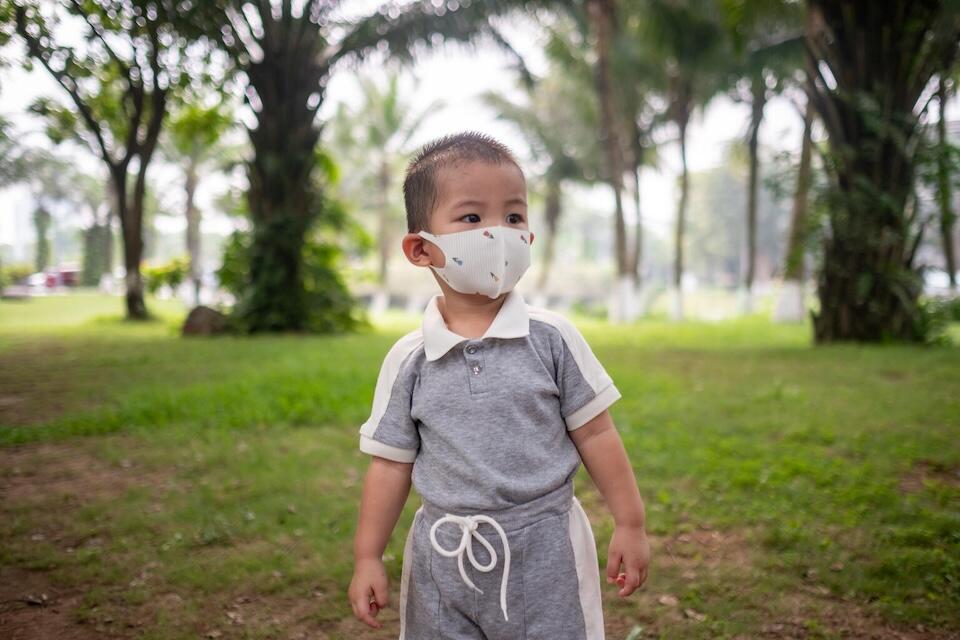 A 3-year-old boy plays at a park in a residential area on the outskirts of Ha Noi, Vietnam wearing a mask due to air pollution in the area.