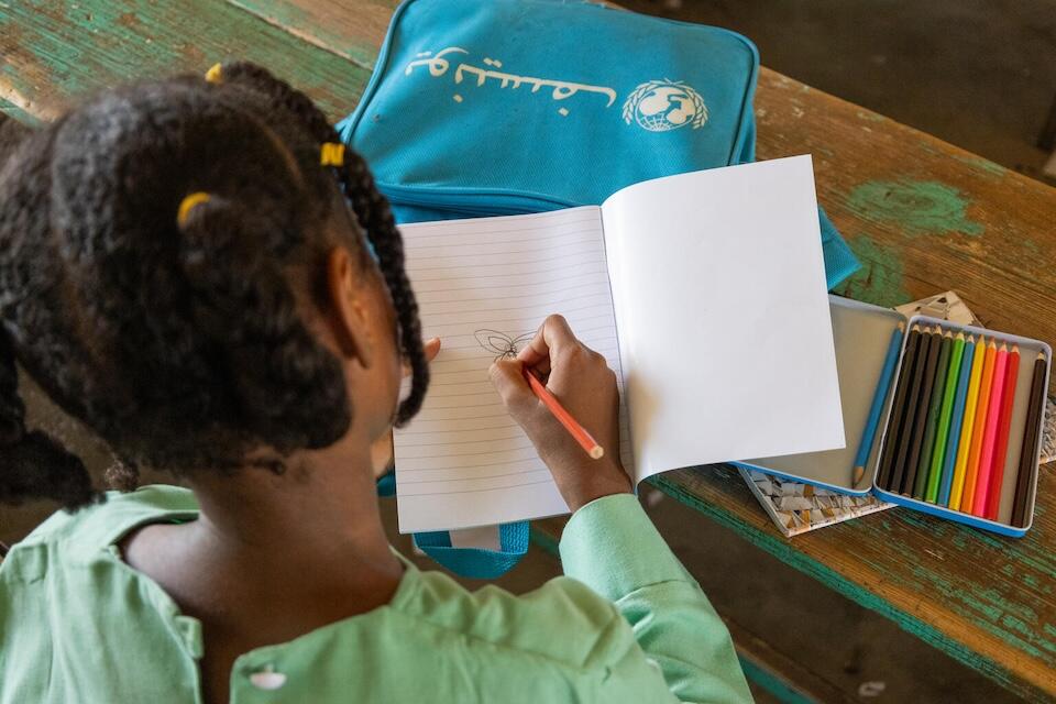 In Port Sudan, Wissam, 9, uses the colored pencils she received from UNICEF to draw a flower in her new notebook.