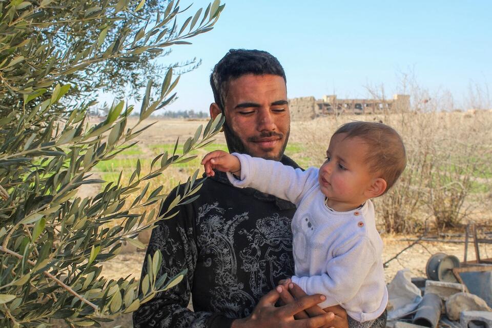 A father holds his 1-year-old son in the yard outside their home in Obada village, Rural Damascus, Syria on Dec. 17, 2024.