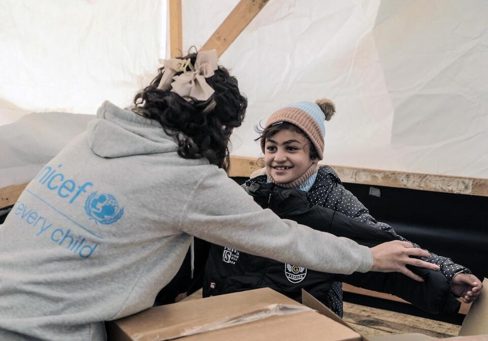 On Dec. 22, 2024, a UNICEF staff member gives warm winter clothes to a child in Al Thapeen Camp, Der Al Balah, Gaza.